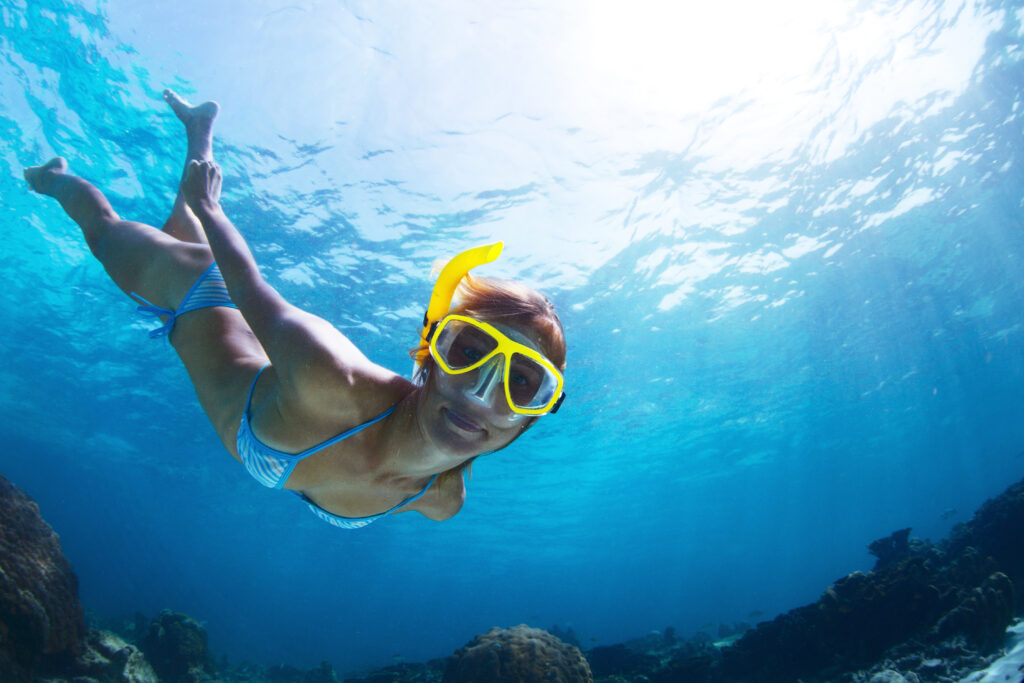 A lady with a yellow snorkel dives deep underwater to look at coral reefs