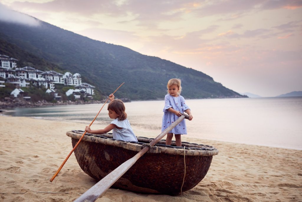 Two children playing in a basket boat on the beach at InterContinental Danang