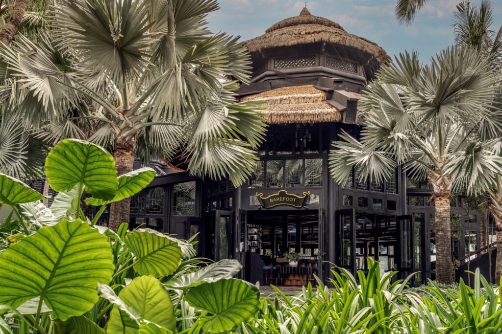 The Entrance of barefoot restaruant with straw thatched roof, jungle plants frame the picture.