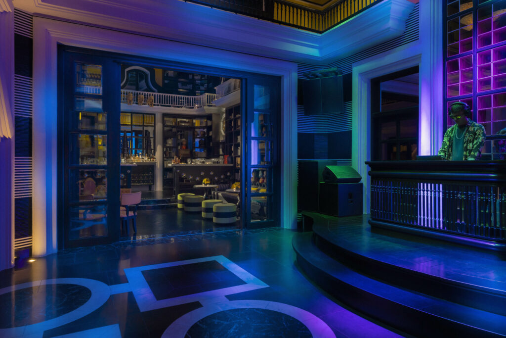 A nightclub dancefloor with a dj and interesting chillout room with monkey statues and bar in background