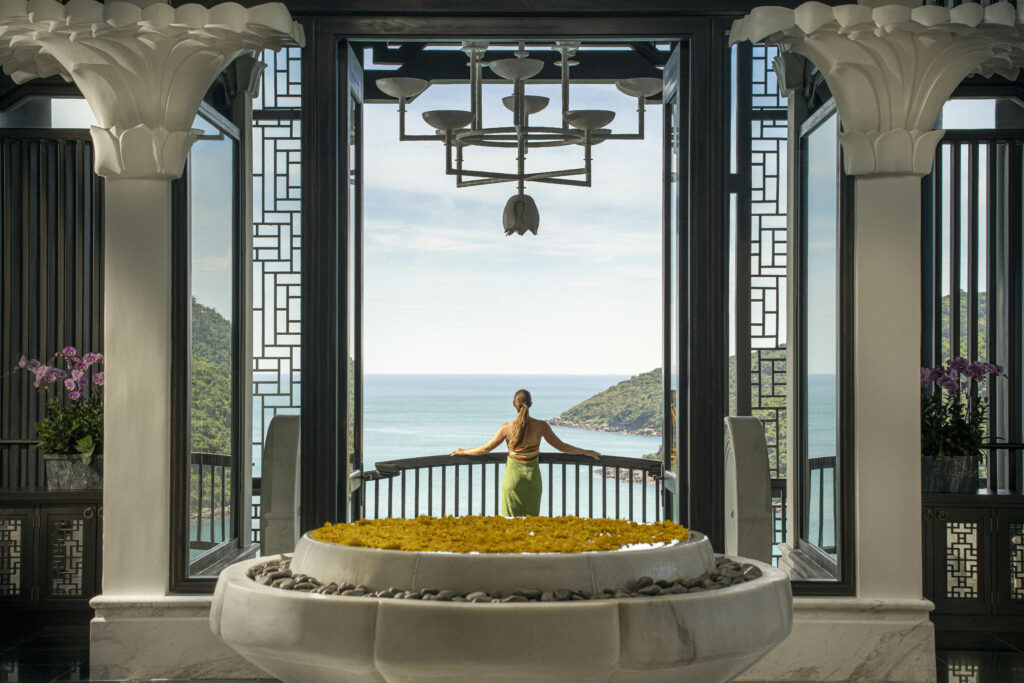 a guest stands in front of a still waterfeature with flowers, and admires the views from the lobby